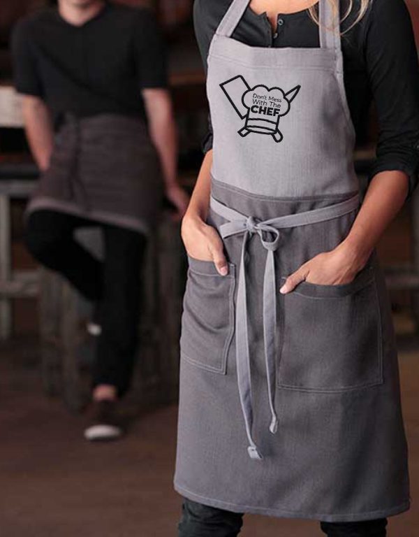 A Woman Wearing an Apron with a Man Behind Her